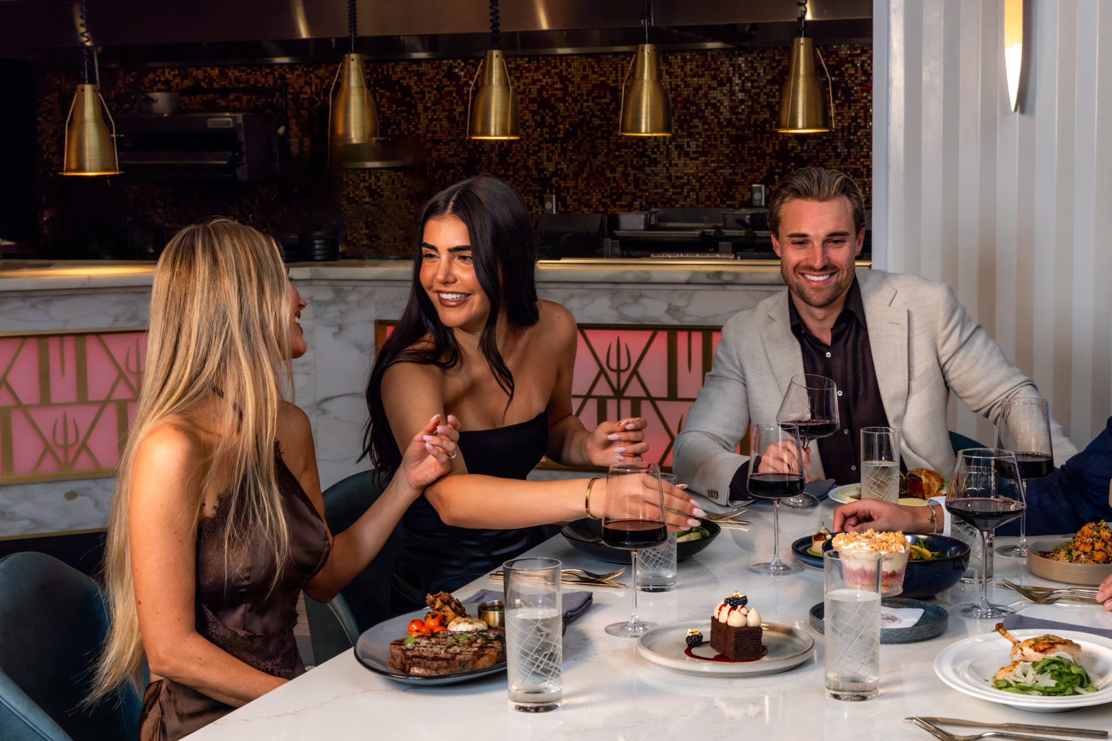 Three friends laughing and talking whilst dining at a restaurant table.