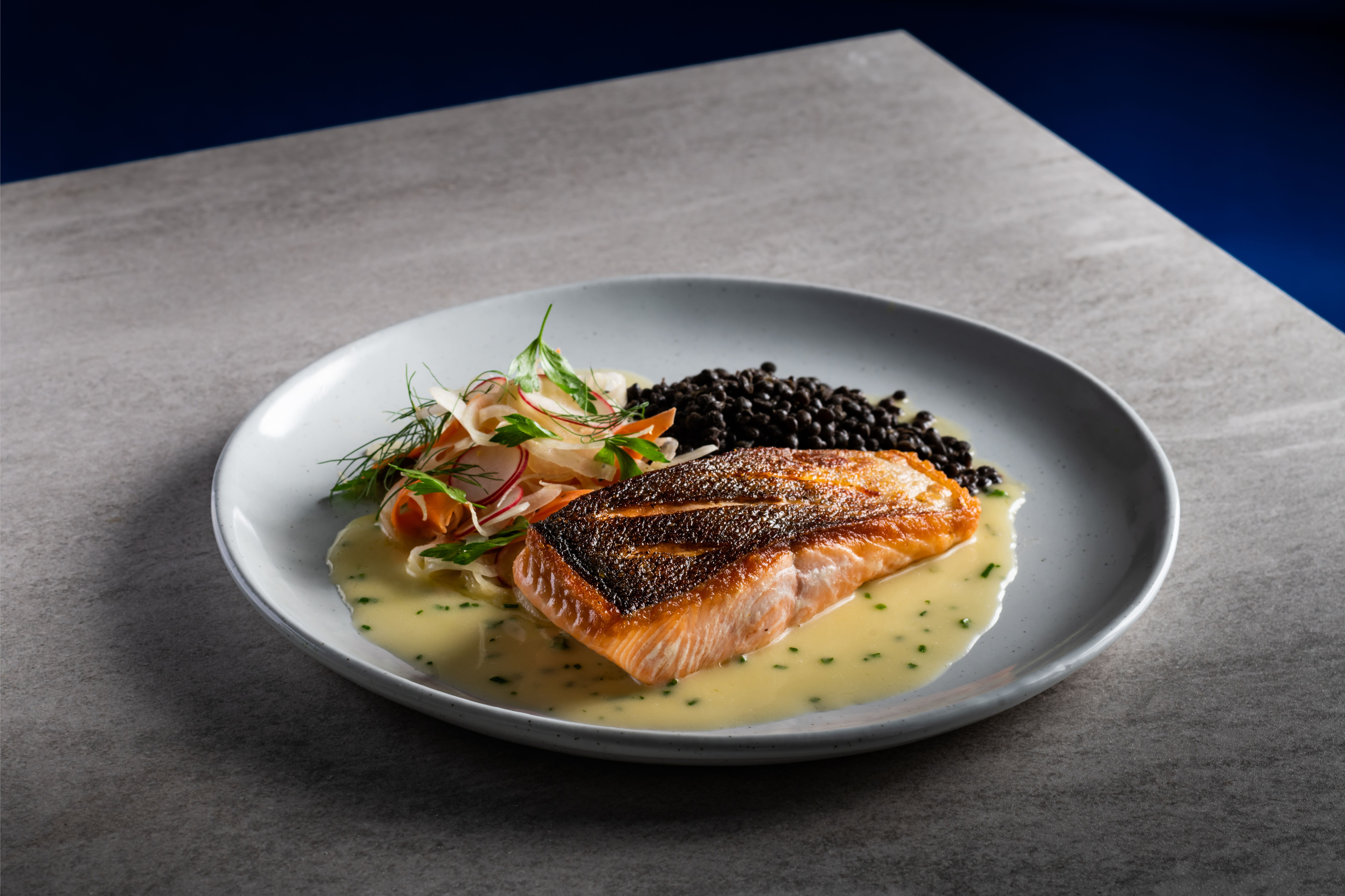 A plate of pan-seared salmon with lentils, a side salad, and sauce.