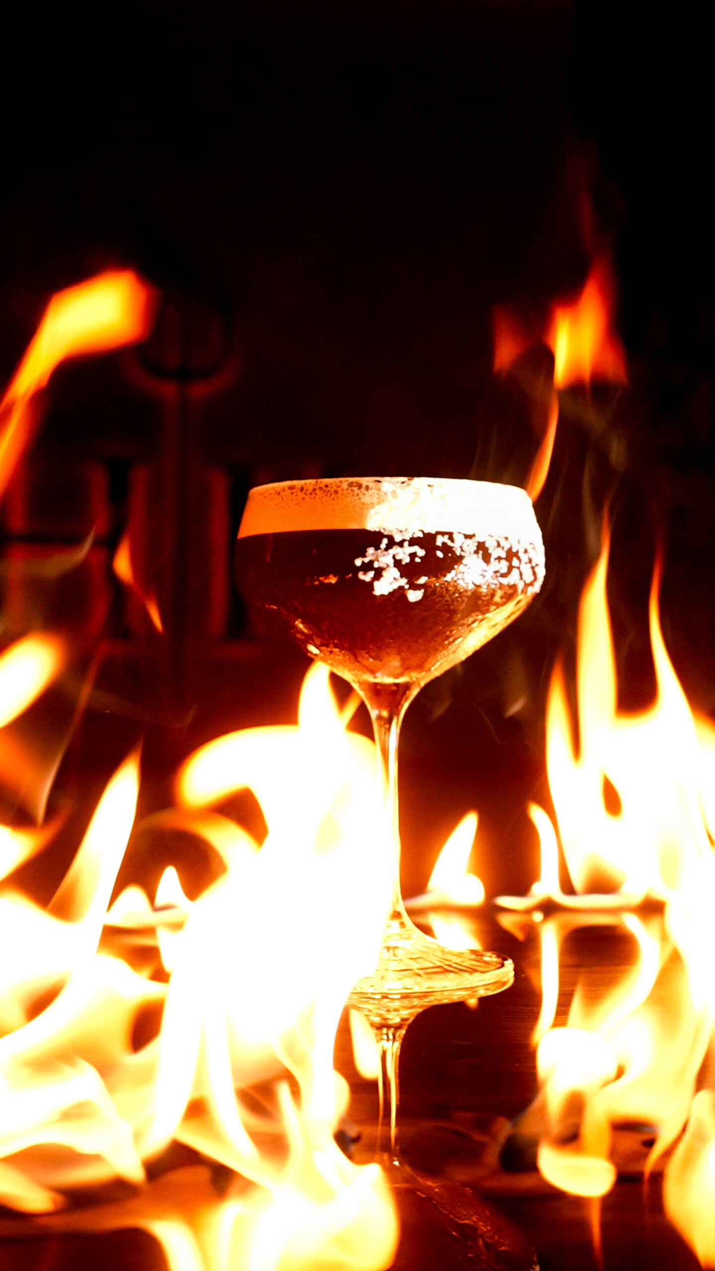 A cocktail in a stemmed glass surrounded by flames.