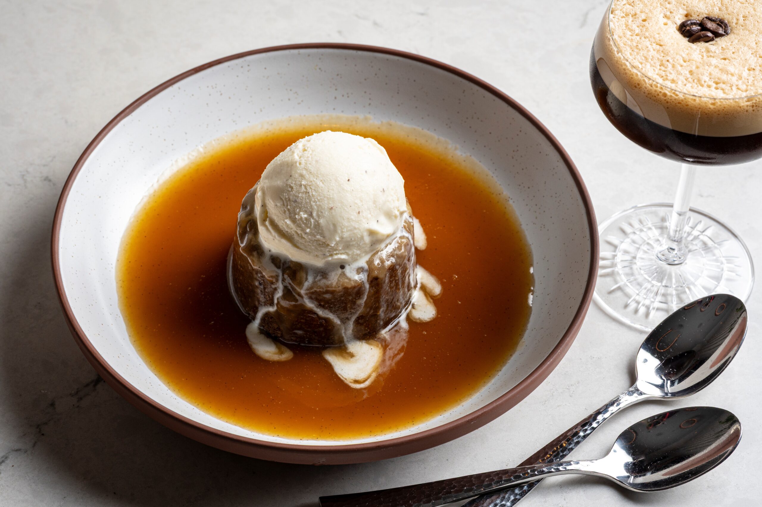 Sticky toffee pudding topped with a scoop of vanilla ice cream in a pool of sauce, served with an espresso martini.