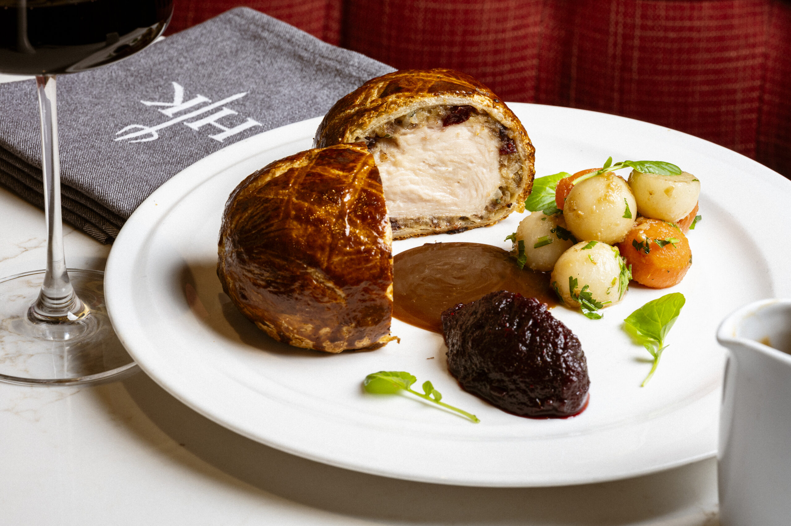 Beef Wellington served with roast potatoes, carrots, and a dollop of relish on a white plate.