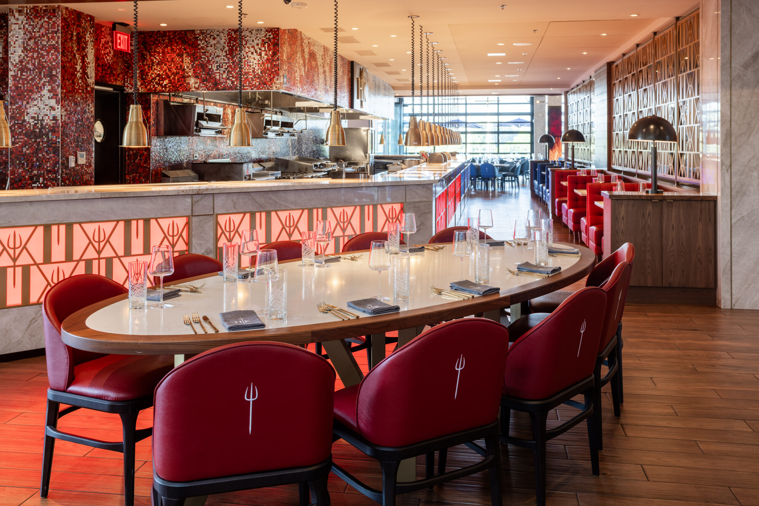 A long oval dining table set for dinner with red chairs in a modern restaurant.