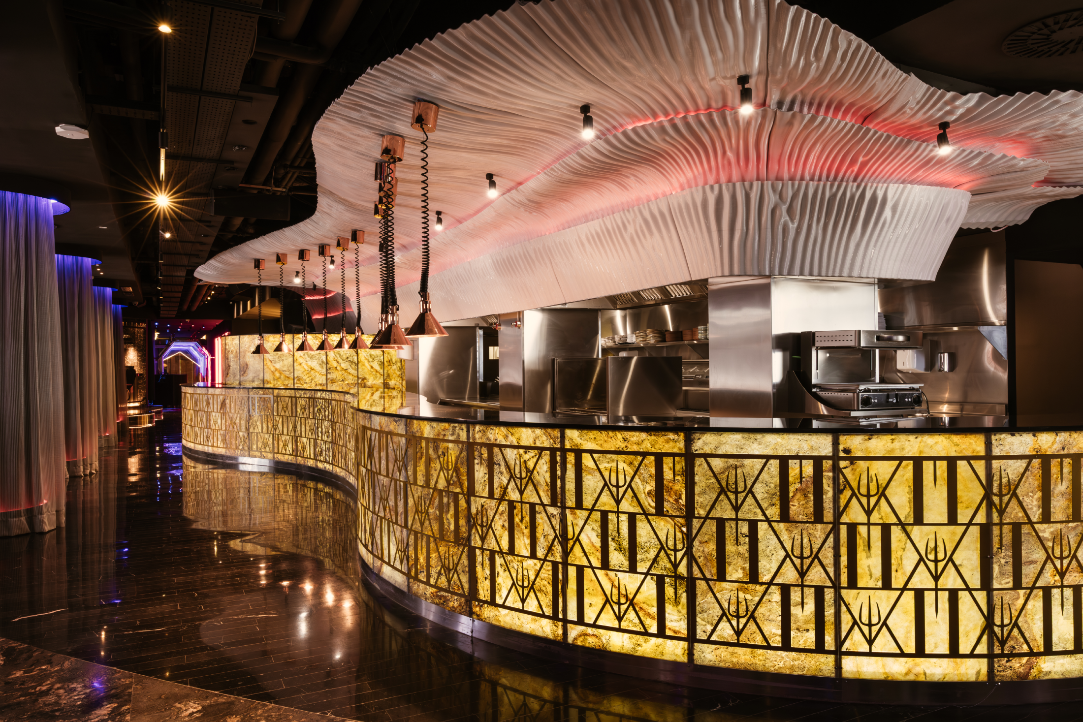 A curved, illuminated bar counter with a geometric metal grille design and a white rippled ceiling feature.