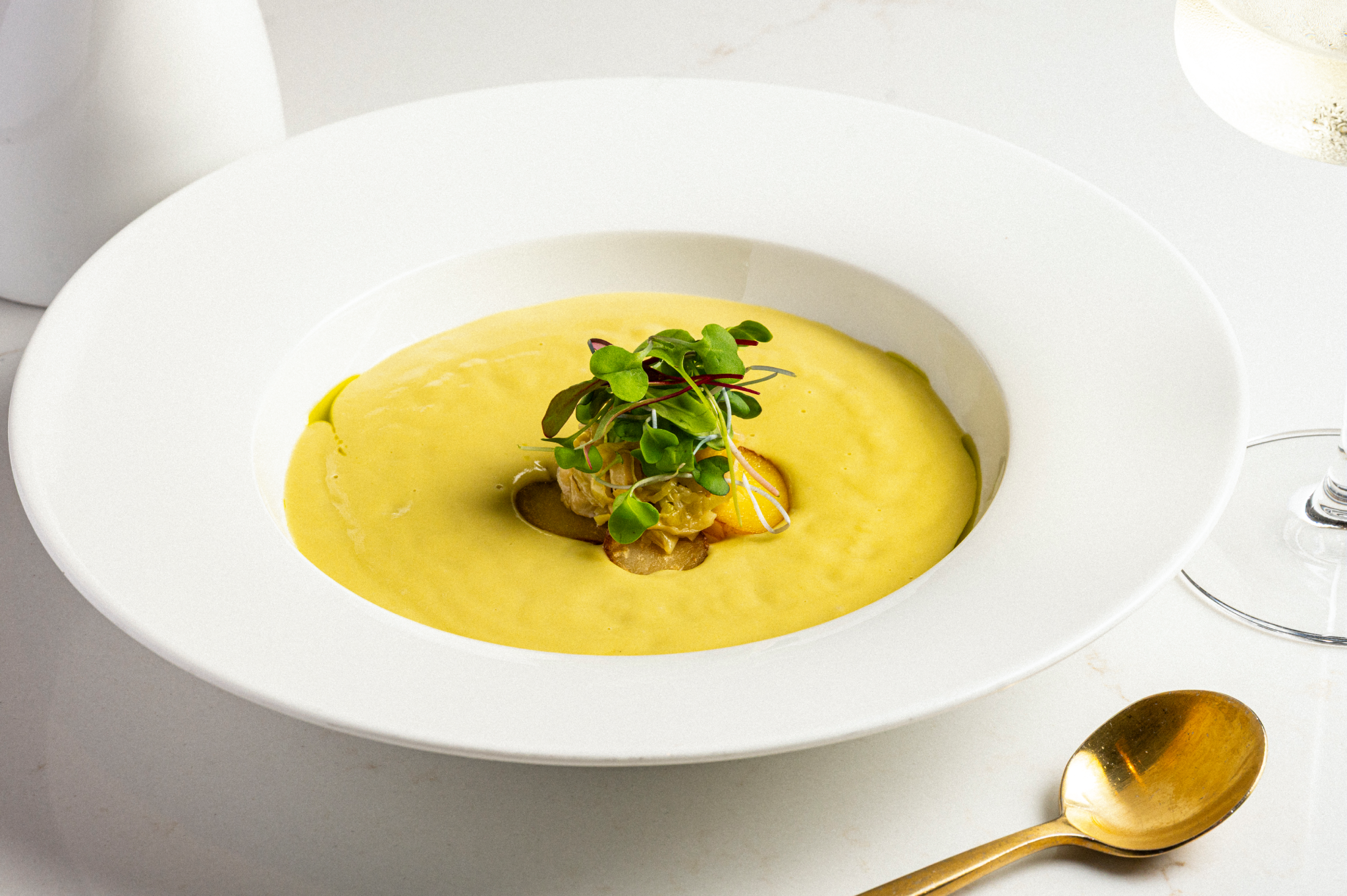 A bowl of yellow soup topped with a garnish of fresh greens.