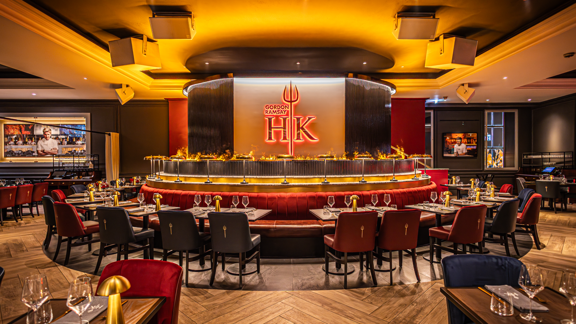 Gordon Ramsay Hell’s Kitchen restaurant interior with a large circular red booth and a glowing trident logo.