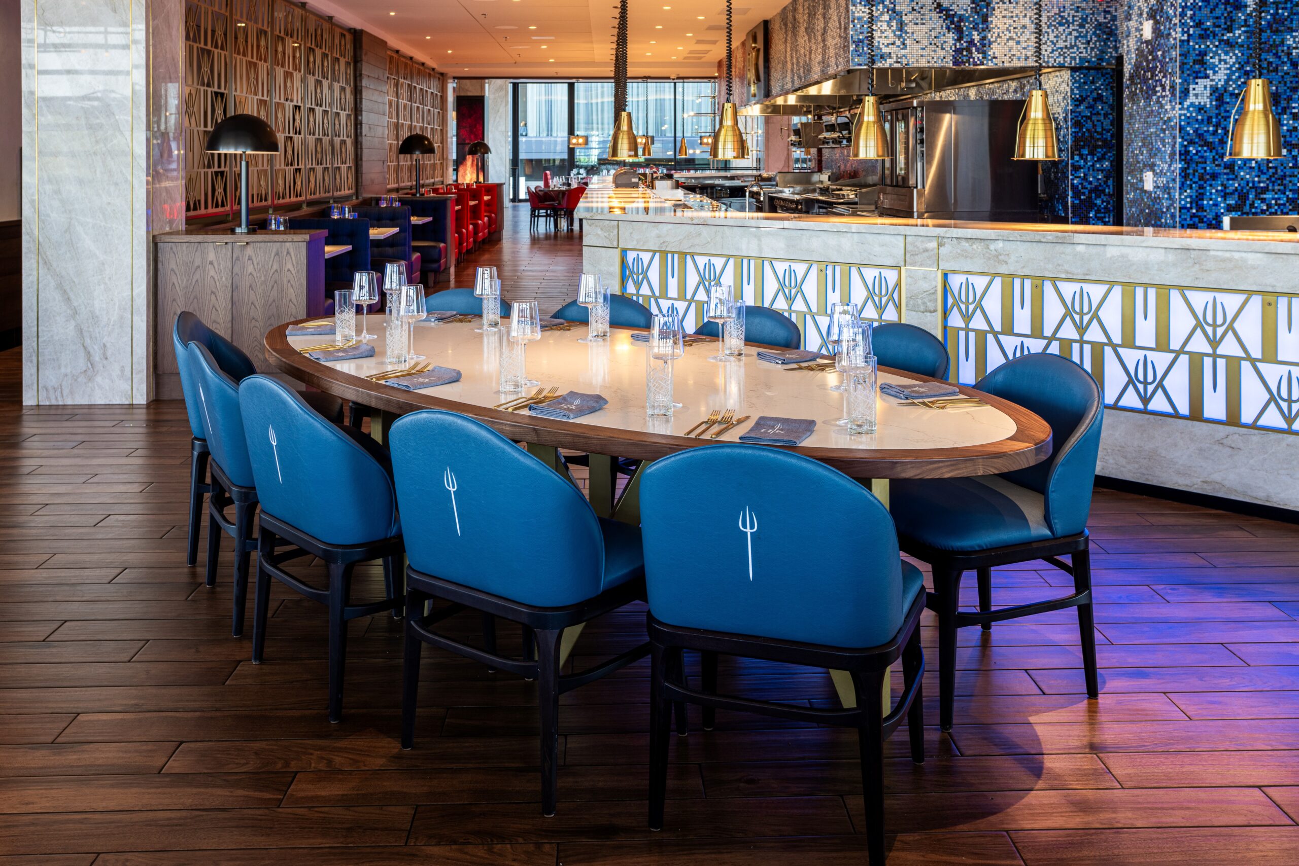 An oval dining table with blue chairs featuring trident logos in a modern restaurant.