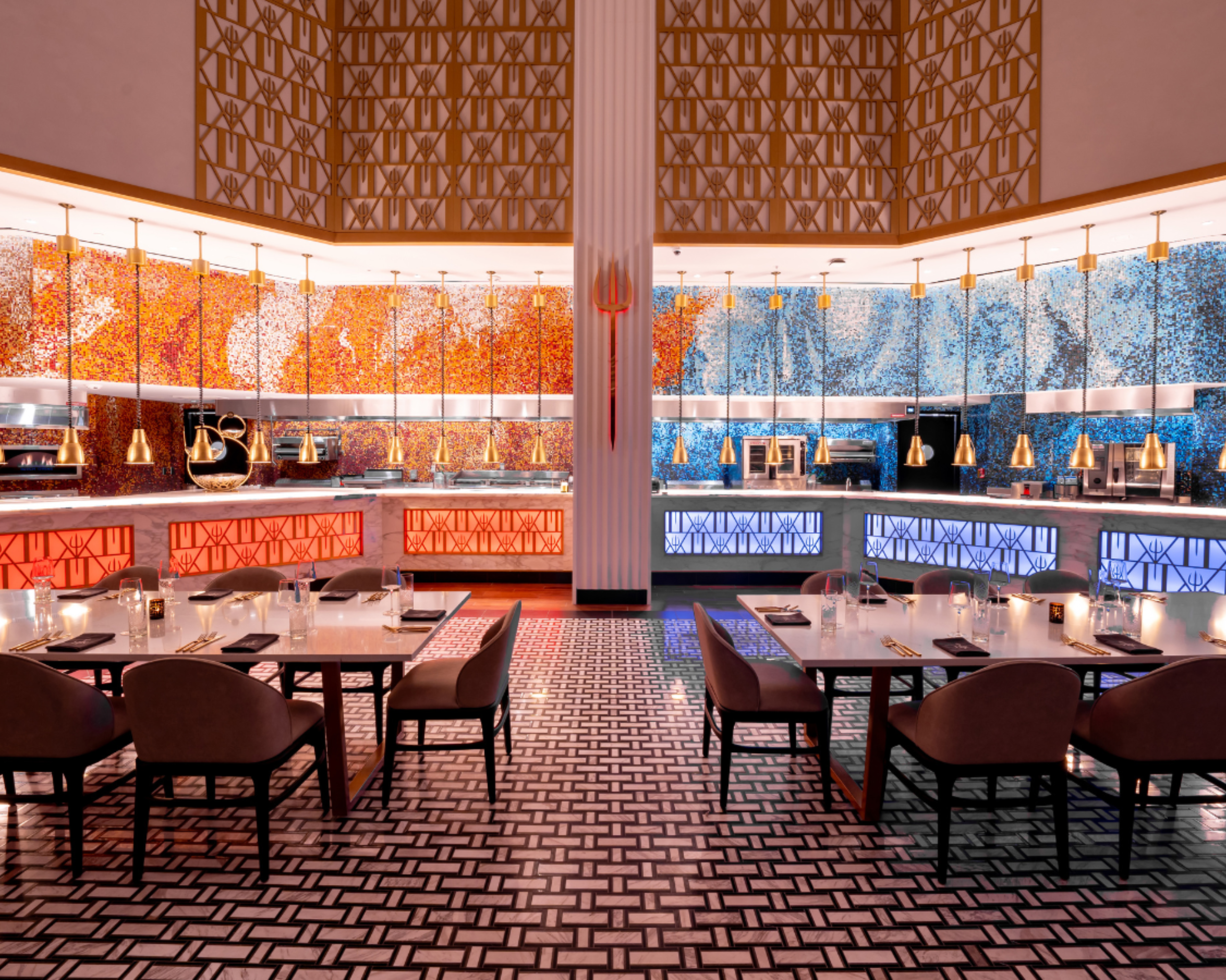 Dining room with two long tables, pendant lights, and a colorful mosaic wall behind the service counter.