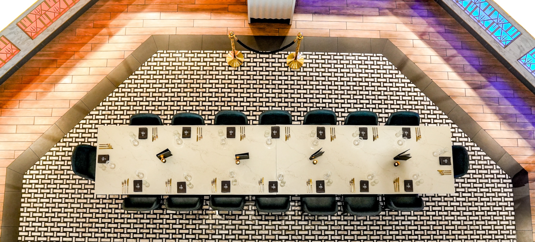 An overhead view of a long rectangular dining table set for twelve on a black and white tiled floor.