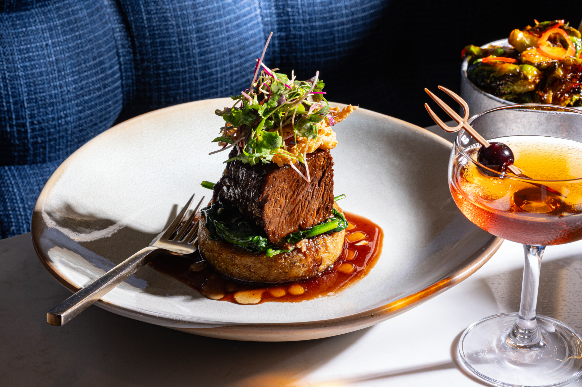 A gourmet steak dish served on a base with salad and a side cocktail.