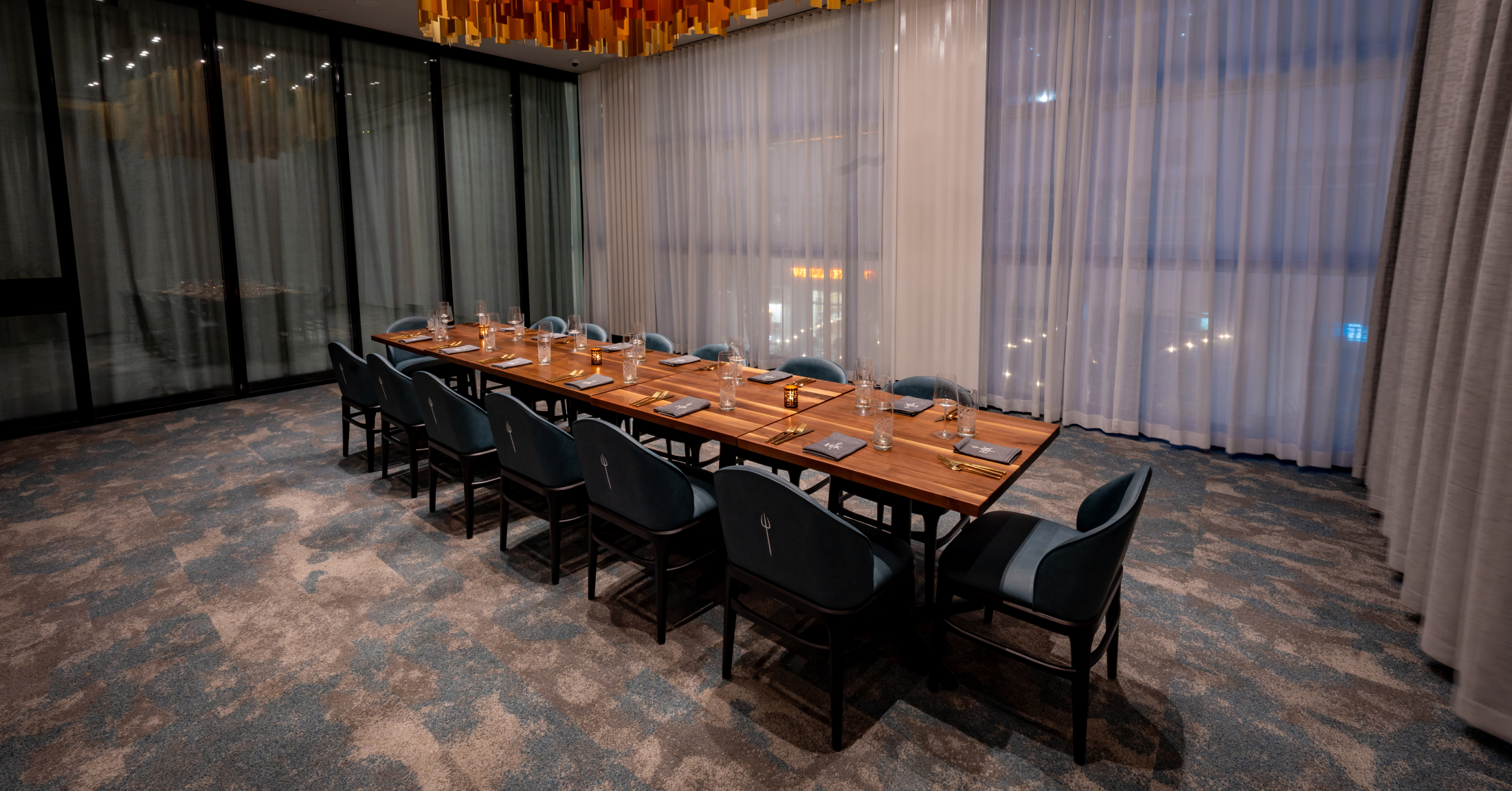 A long wooden dining table set for a formal dinner with dark chairs in a private room.