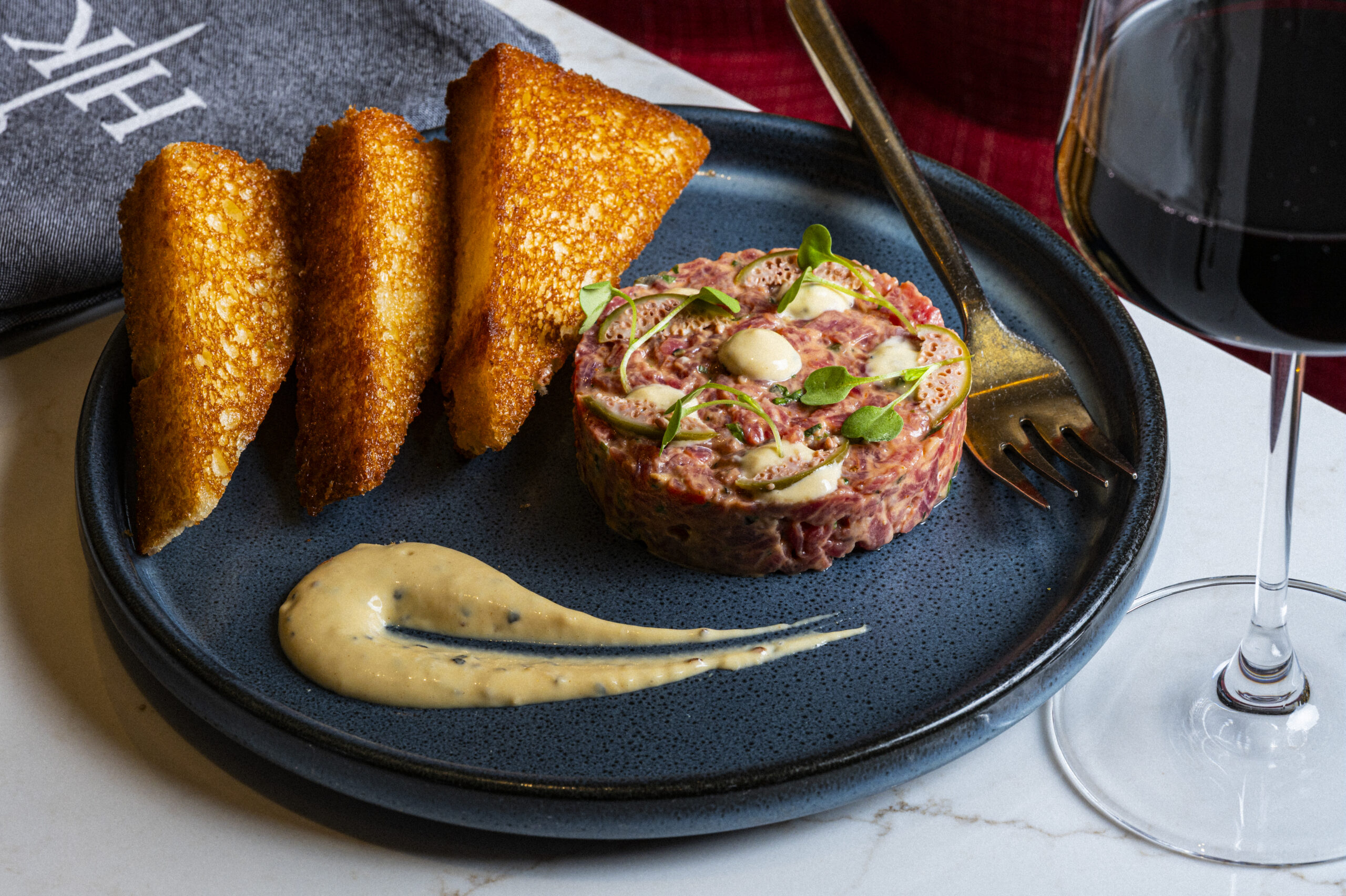 Beef tartare with toasted bread, a sauce swirl, and a glass of red wine, perfect for private dining.