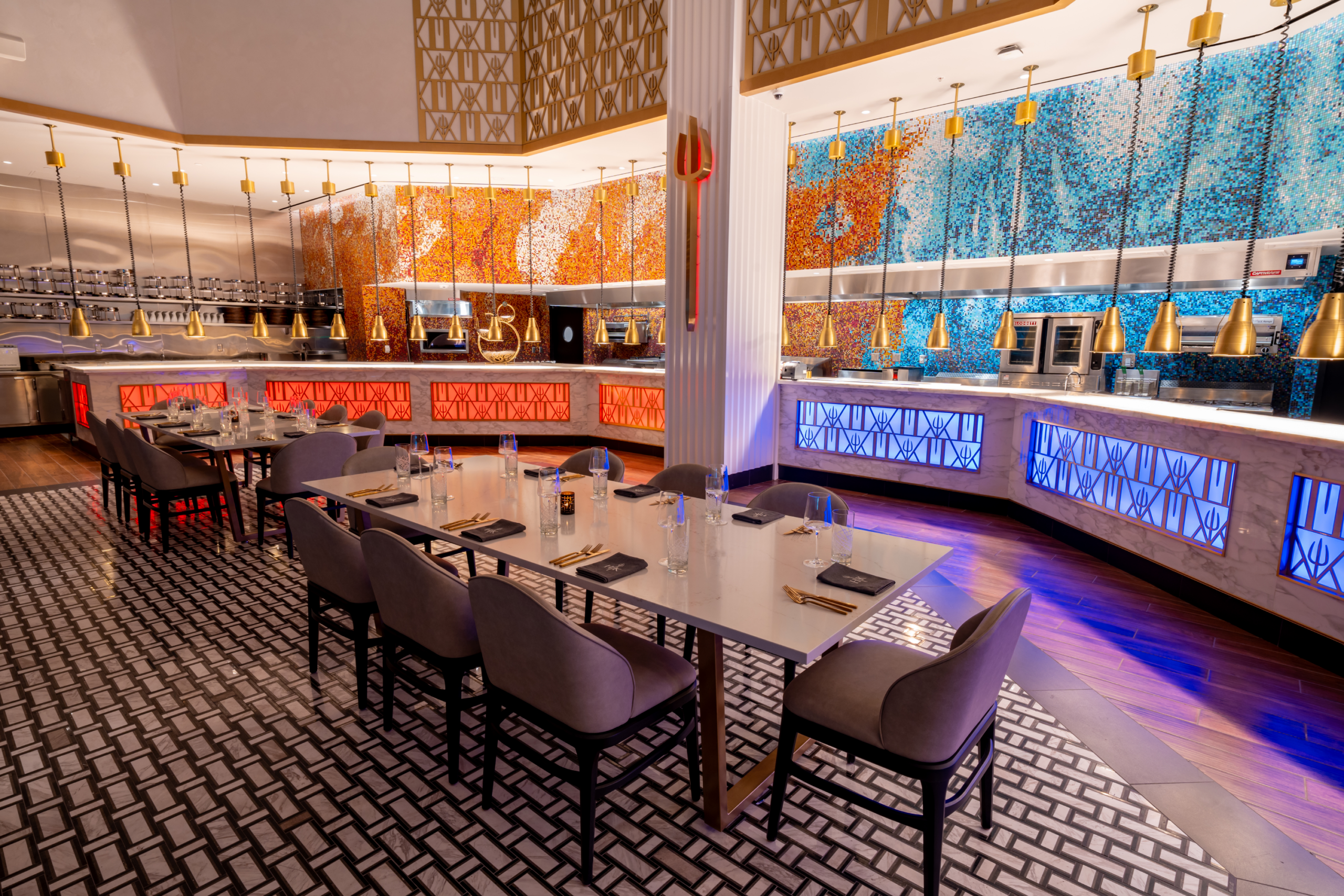 Empty dining tables with place settings in a restaurant with vibrant mosaic walls and pendant lighting.
