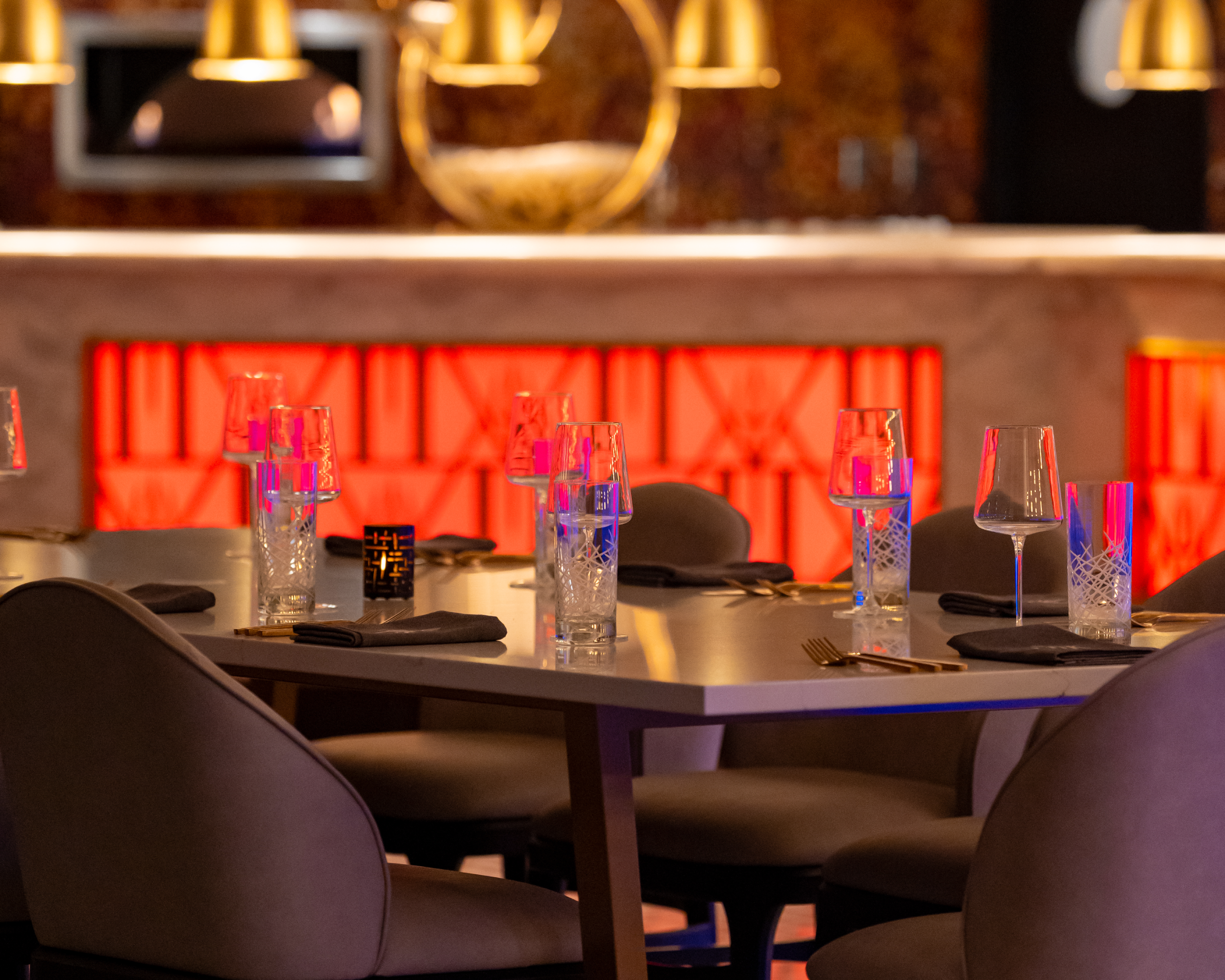 A restaurant dining table set with glassware, serviettes, and cutlery in front of a backlit red decorative screen.