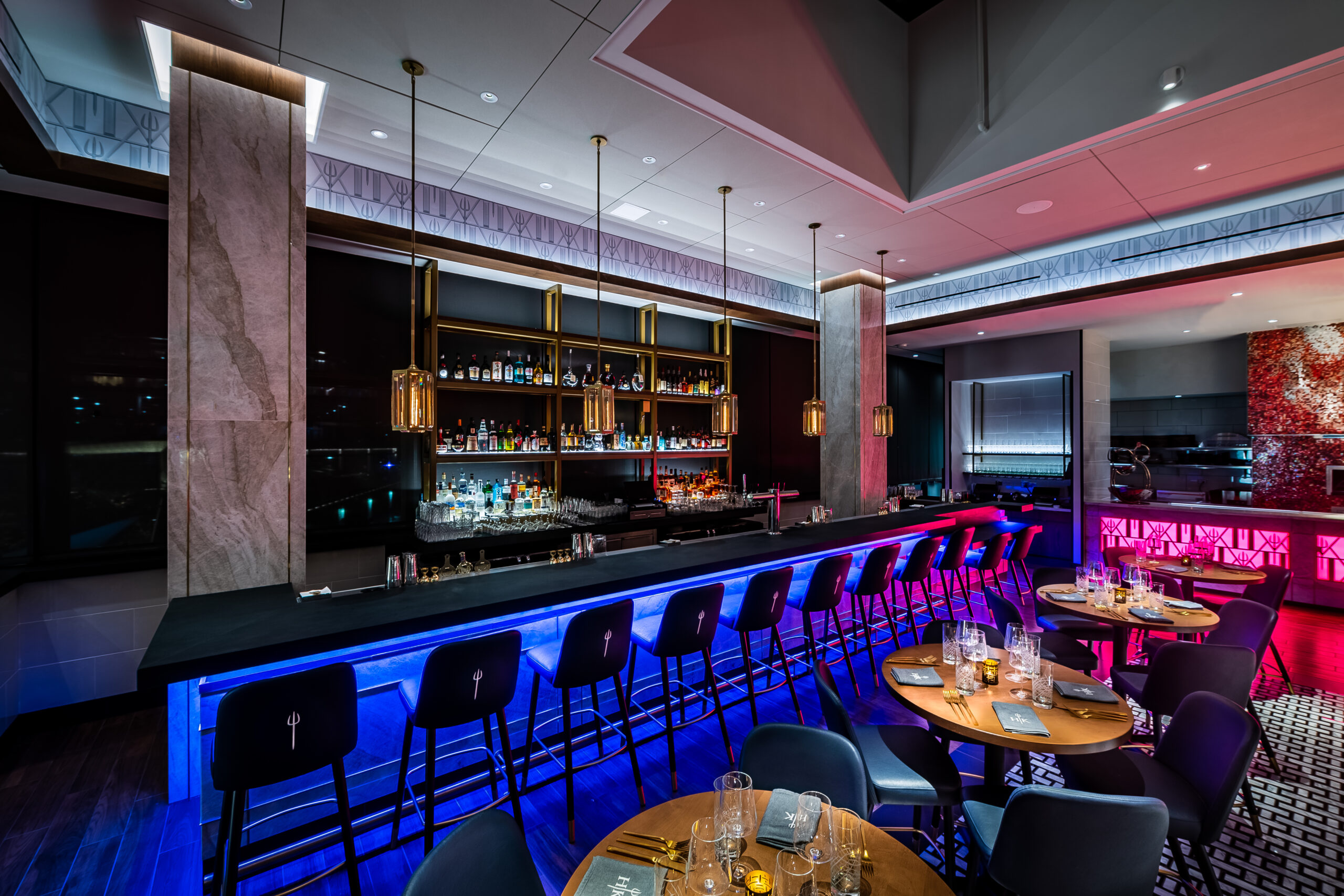Modern Hell’s Hideaway bar with blue under-counter lighting, stools, and tables set for dinner.