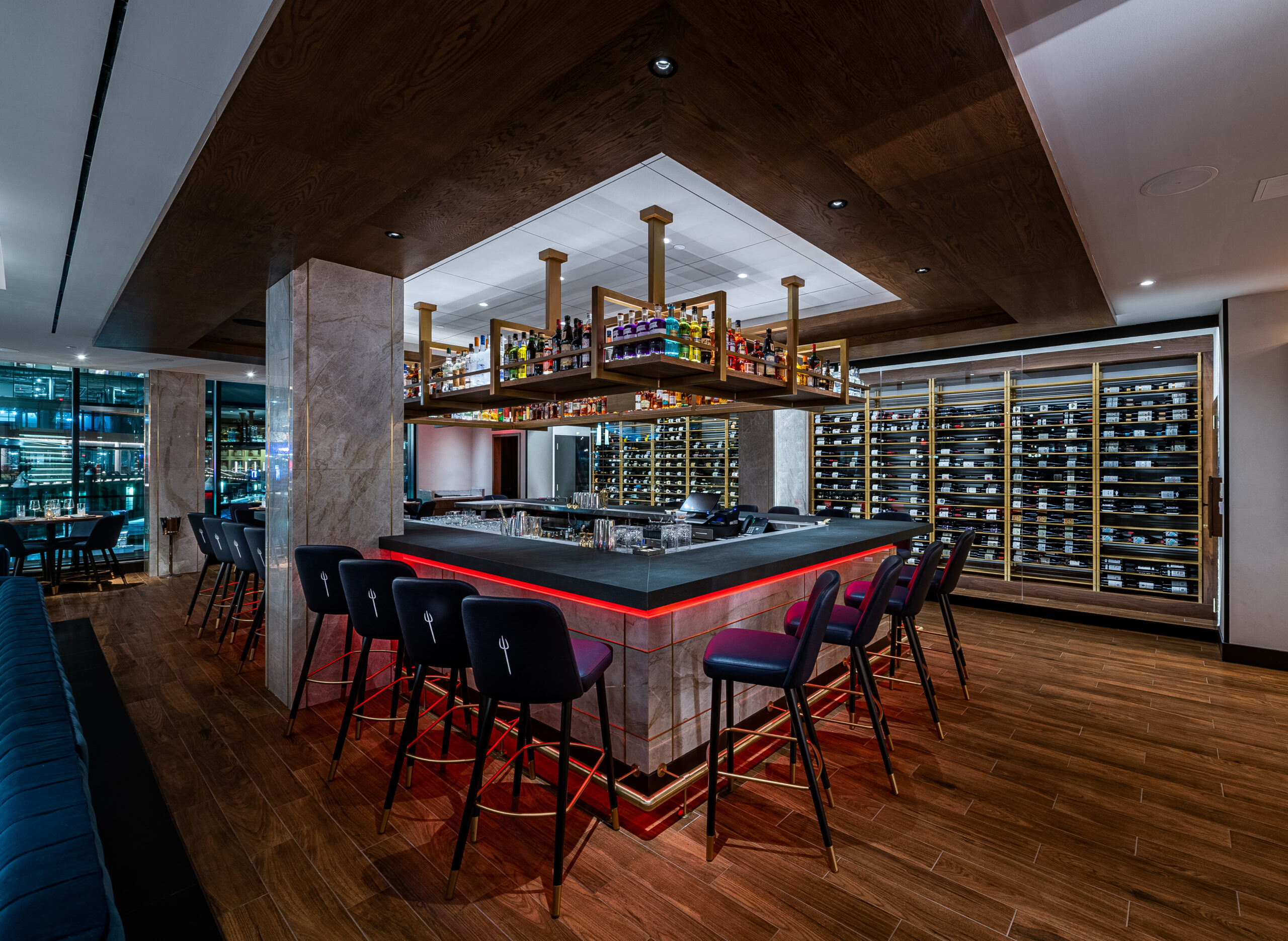 Modern bar at Hell’s Hideaway Private Dining Miami with a central island, hanging spirits display, and wine racks.