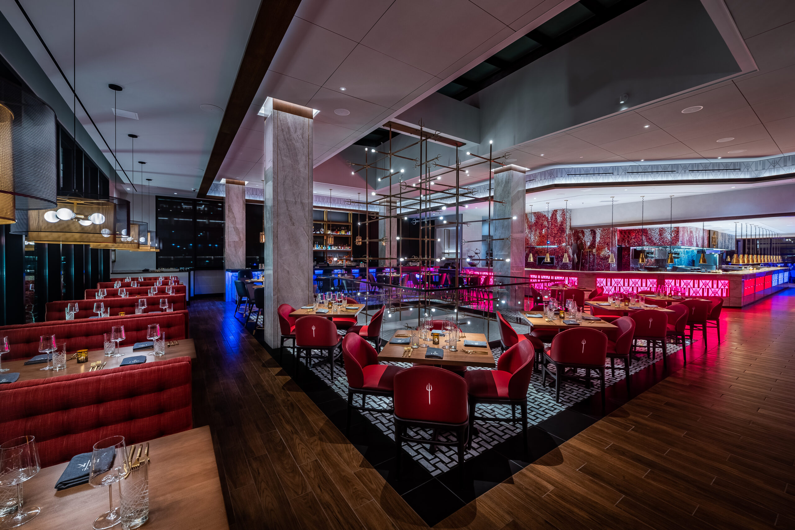 Modern restaurant dining room with red chairs, wooden tables, and ambient purple and red lighting.